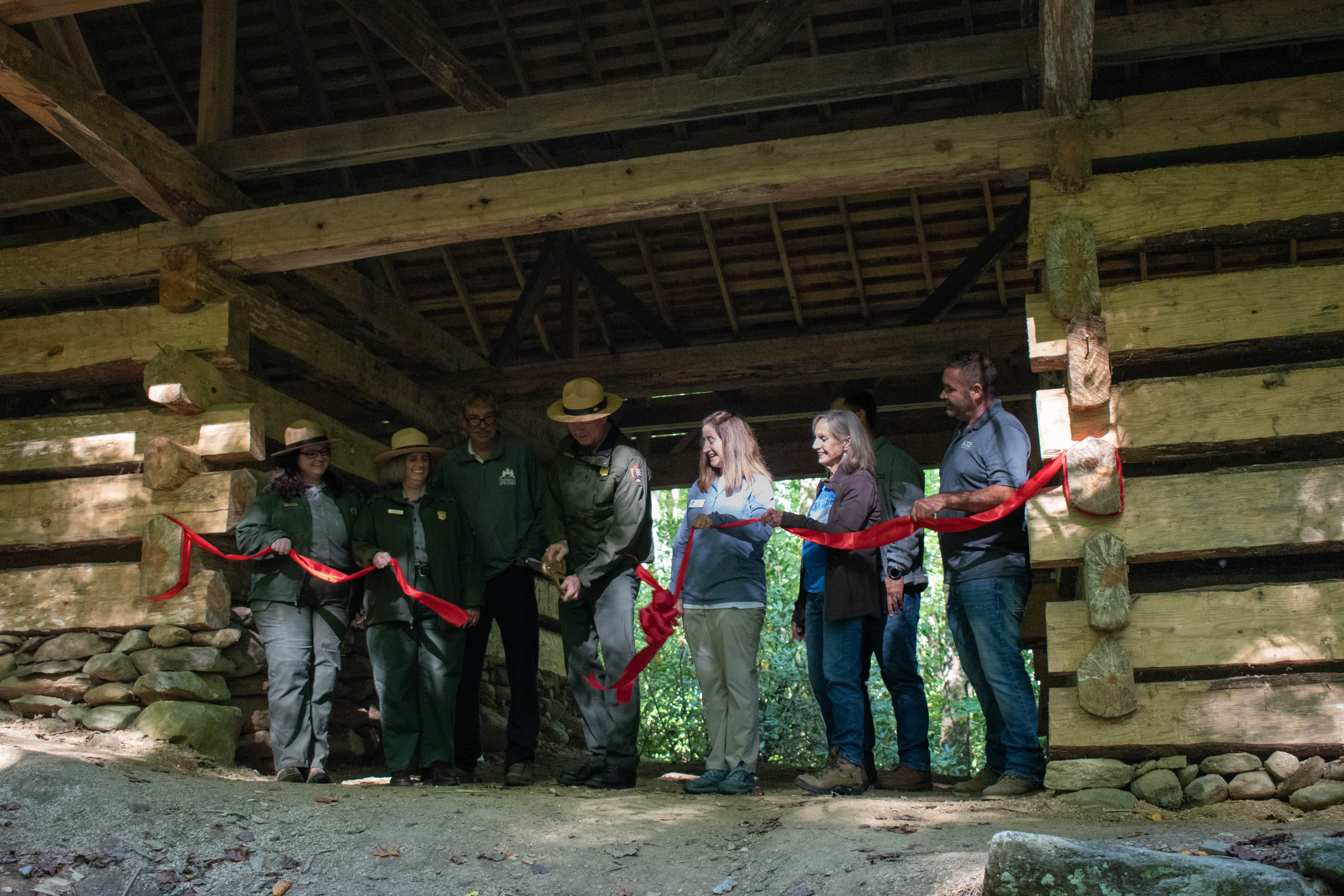 A group of people cuts a ceremonial red ribbon while standing inside a newly-built historical barn