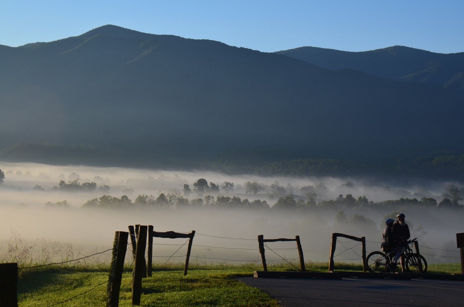 Two people by fence in cades cove on bicycles