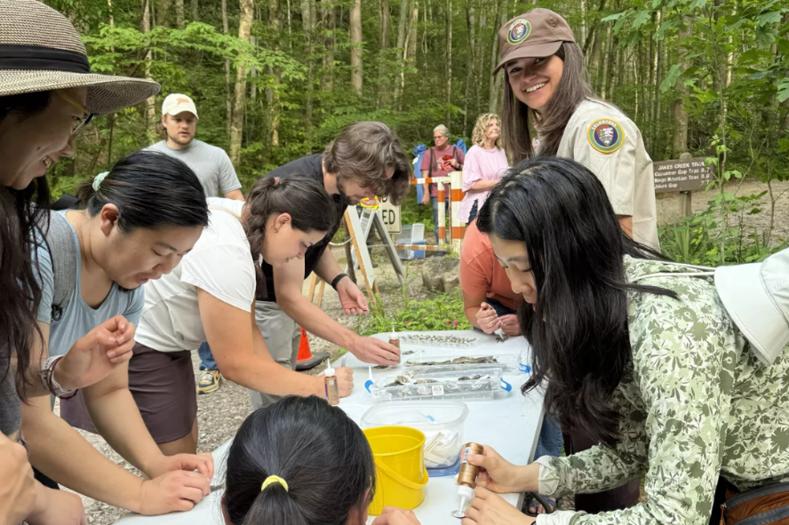 A volunteer with several park visitors creates art at a table.