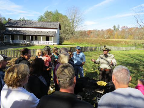 National Park Service Volunteer Ed Langston talks with visitors with a mountain scene and historic building in the background.