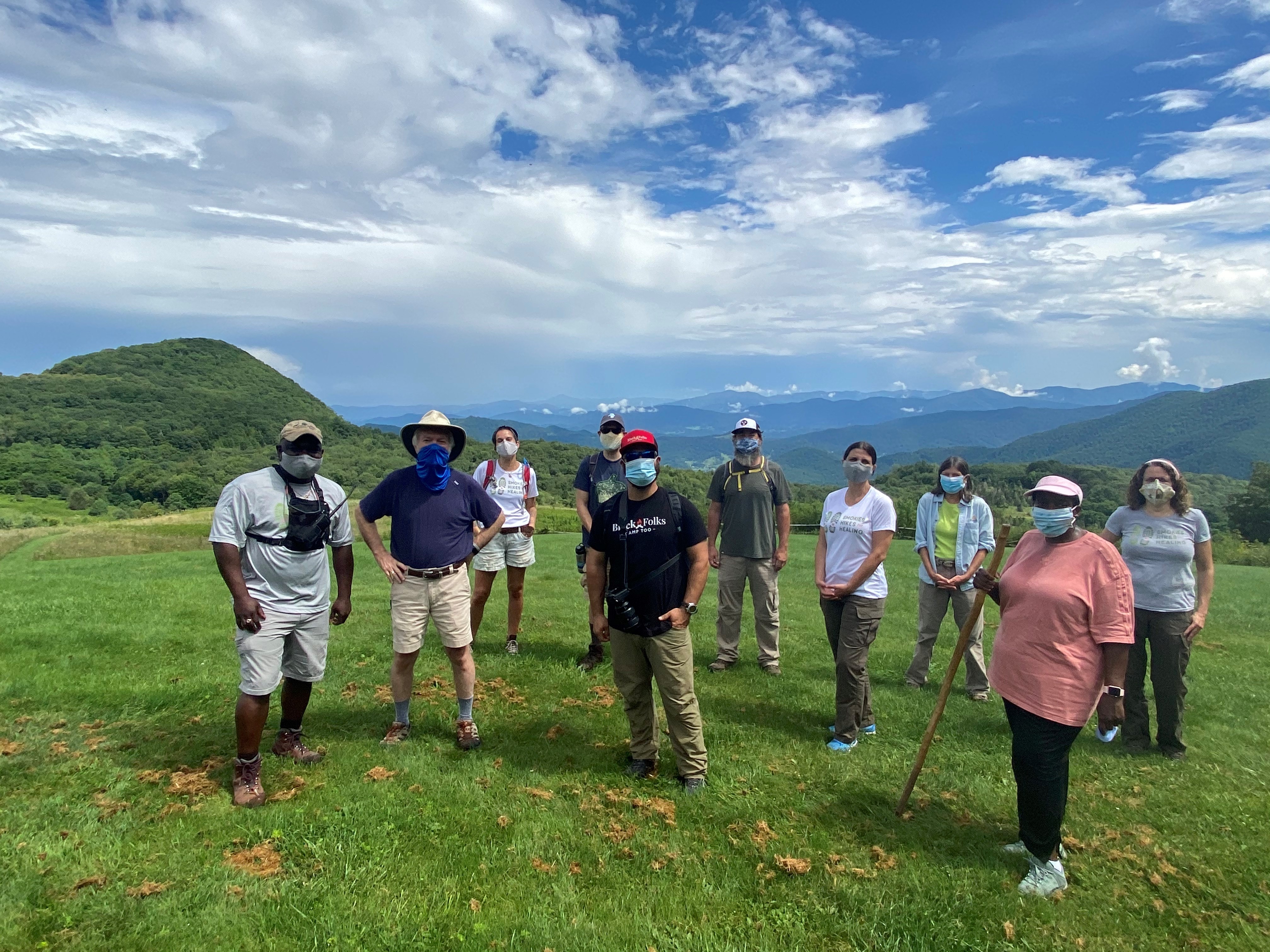 A group participating in one of the Smokies Hikes for Healing, 2020 A group of people standing in an open field with mountains in the background.