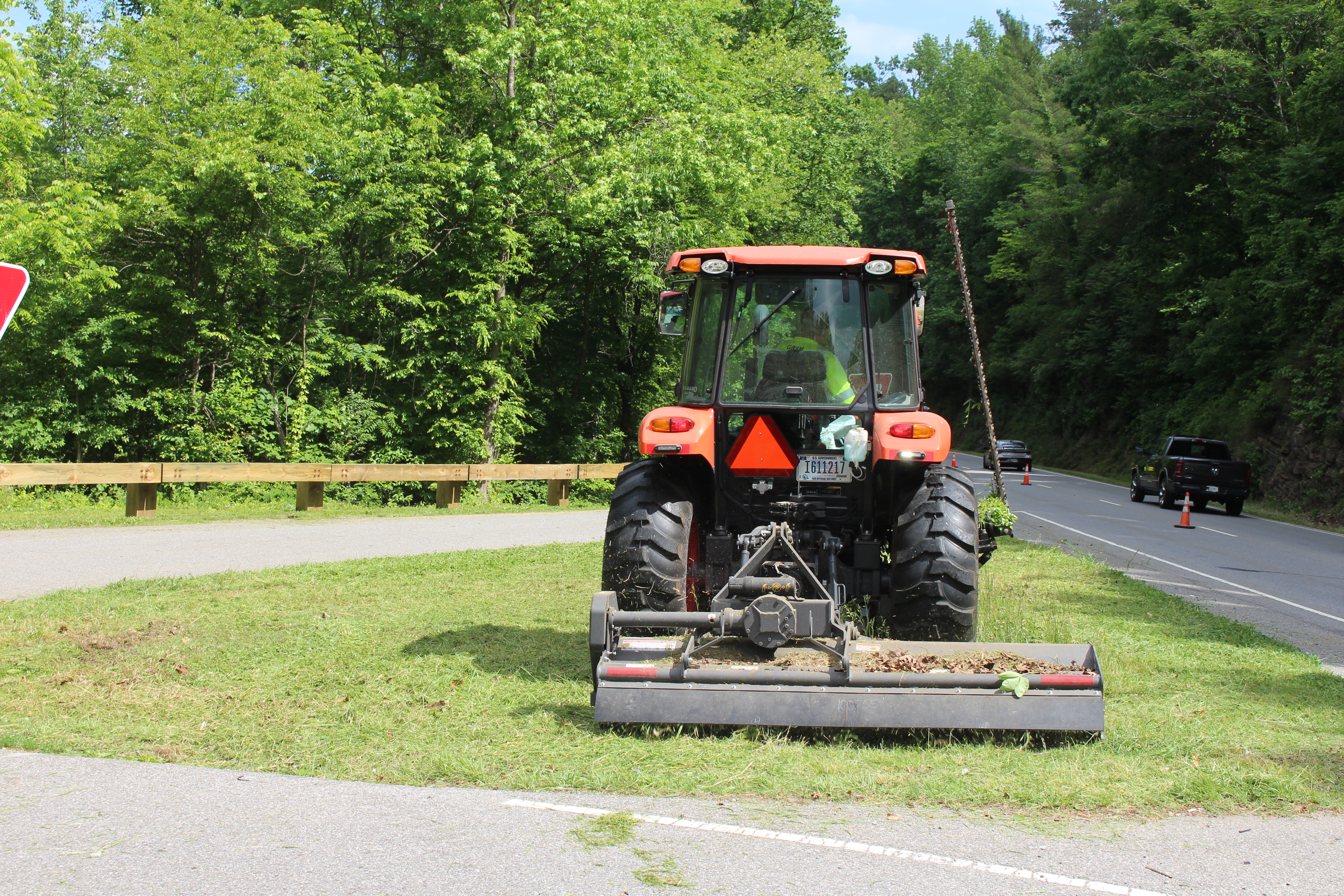 A large tractor mows grass along a busy road.