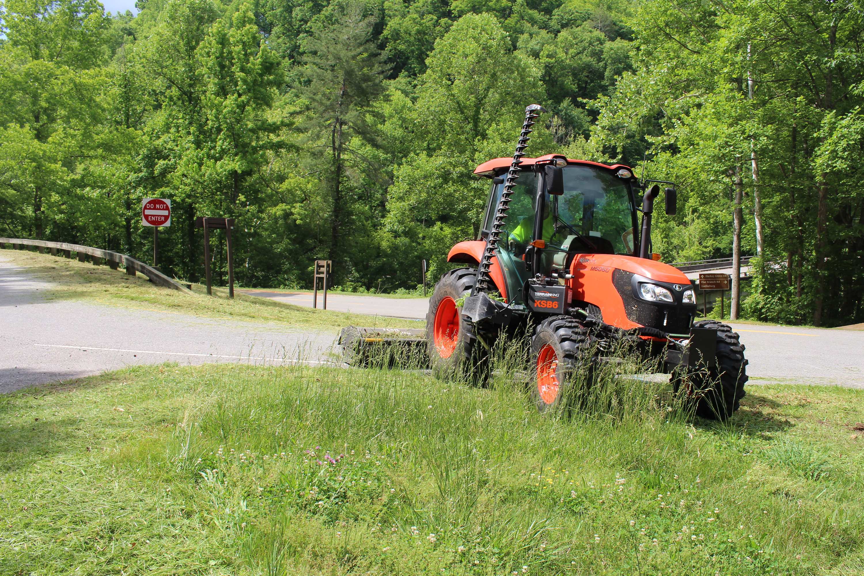 A tractor mowing grass on a road.