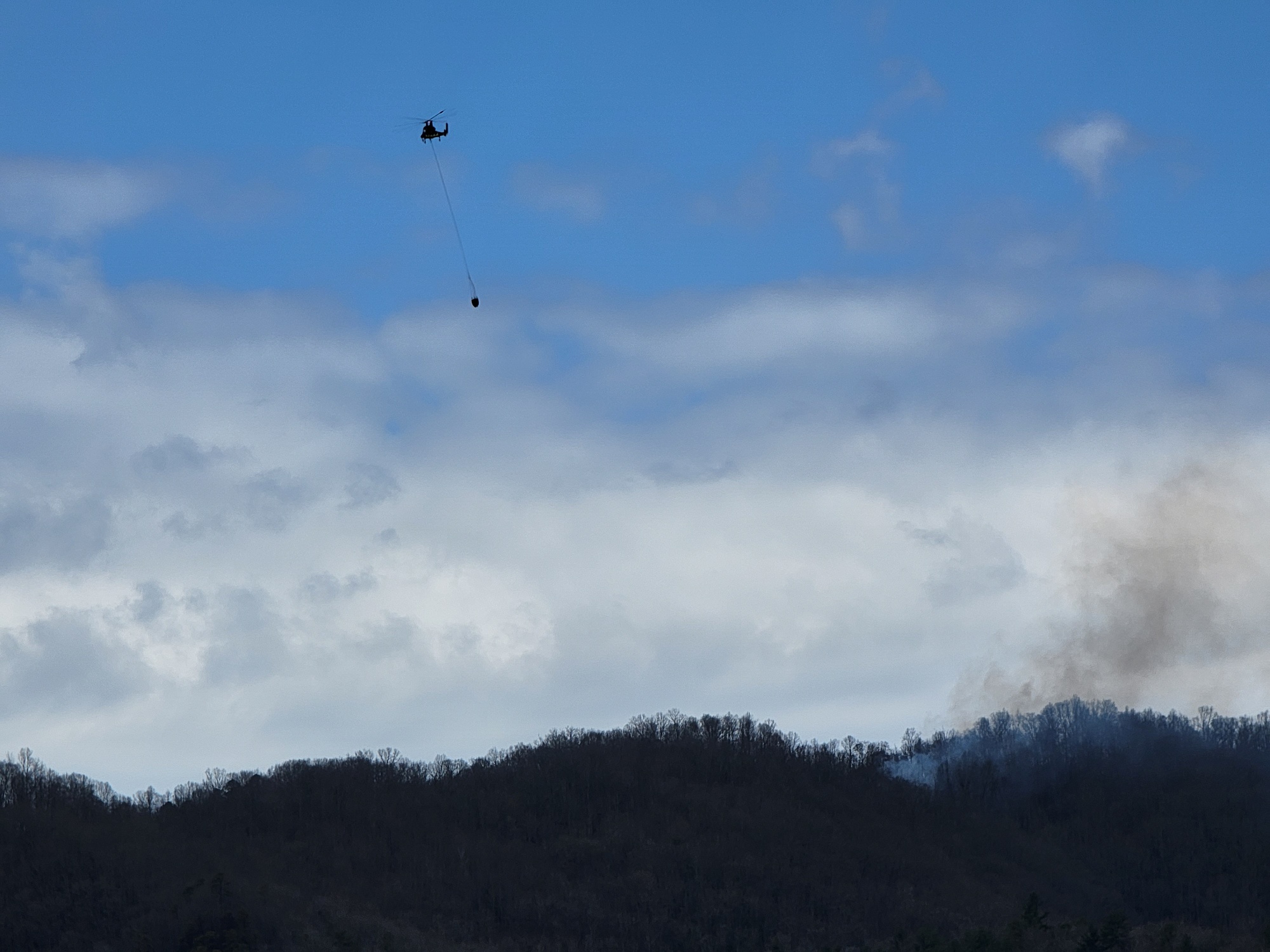 Thomas Divide Complex Air Support Helicopter flying over the complex fire with a water bucket dangling from the underside of the helicopter.