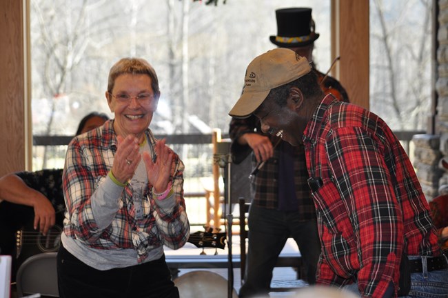 Two people smiling and clapping along to live music. A person in the background is playing a violin.