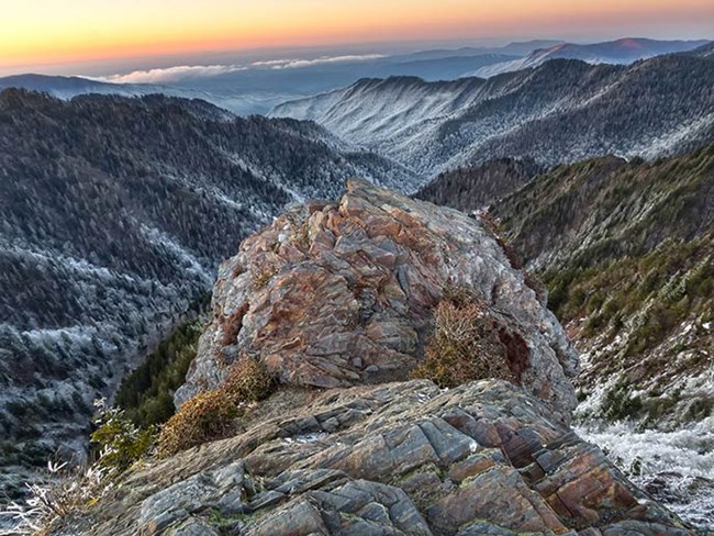 A craggy, rock promontory overlooks snow covered mountains and valleys.