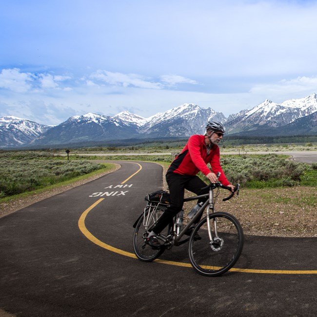 Cyclist riding on the Grand Teton Pathway with the Teton Range in the background