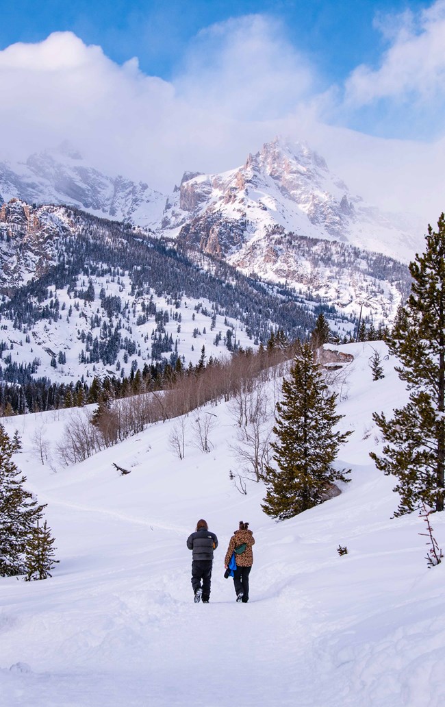 Visitors hiking on a snow-covered path towards Taggart Lake and the Teton Range