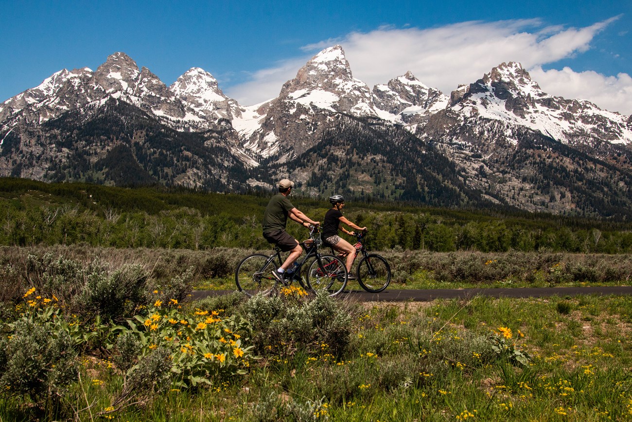 Two bikers ride along Grand Teton's multi-use pathway and gaze at the Tetons