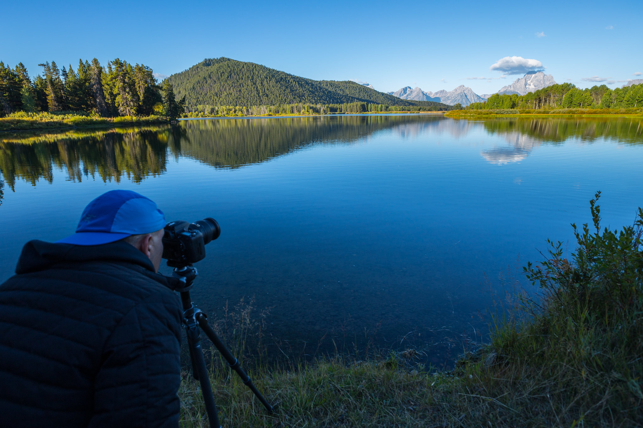 photography A photographer looks at the Tetons over a lake.