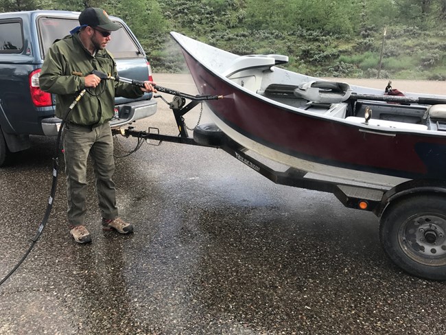 Employee power-washing a drift boat to remove any potential aquatic invasive species (AIS)
