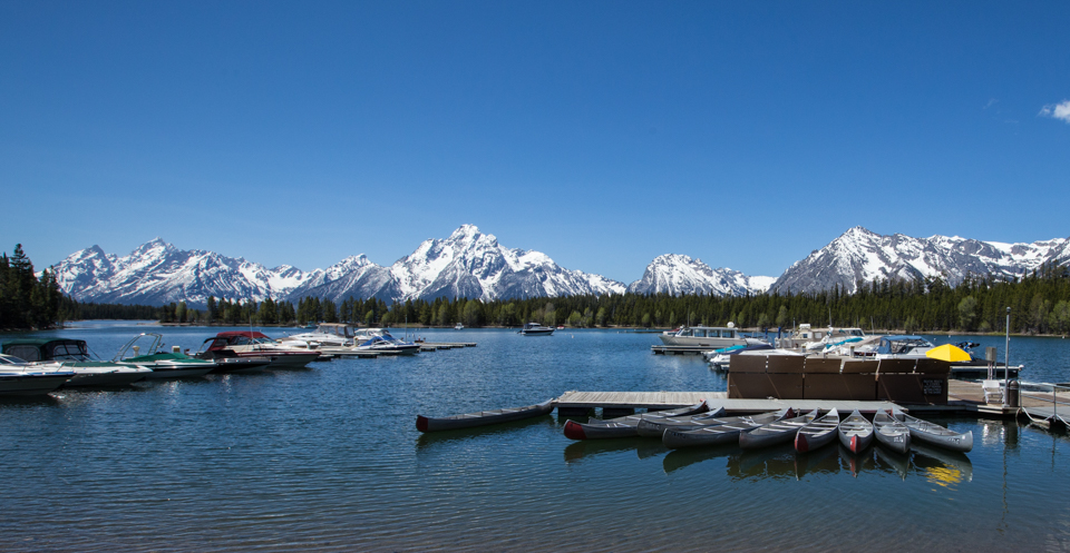 View of motorized boats and canoes in the water at the Colter Bay Marina with the Teton Range in the background.