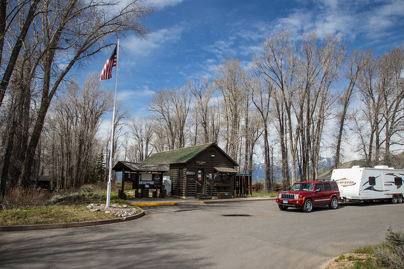 Park Campground check in cabin with American flag in front and truck and camper trailer parked in front with cottonwoods surrounding.