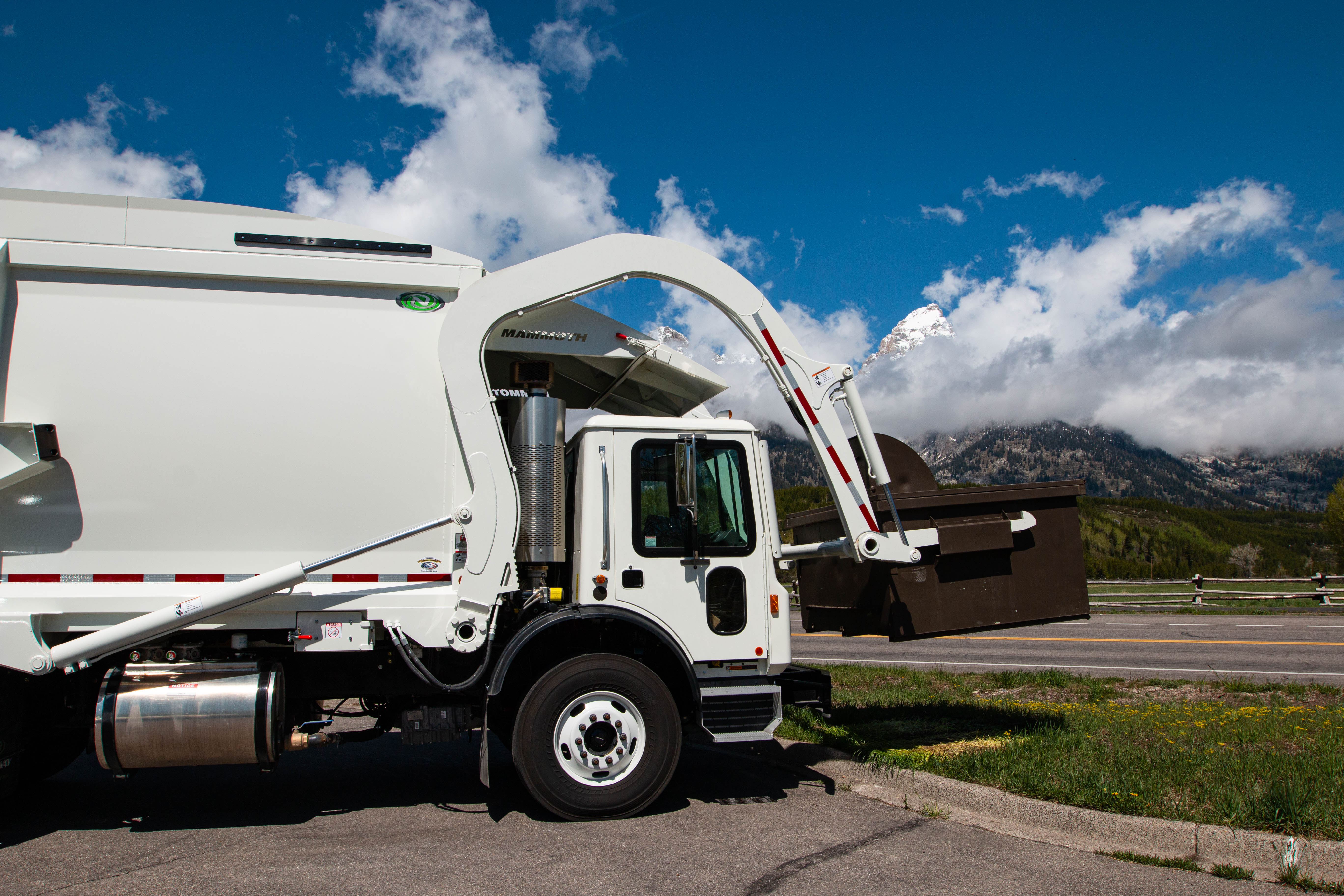 a garbage truck lifting a dumpster in front of mountains