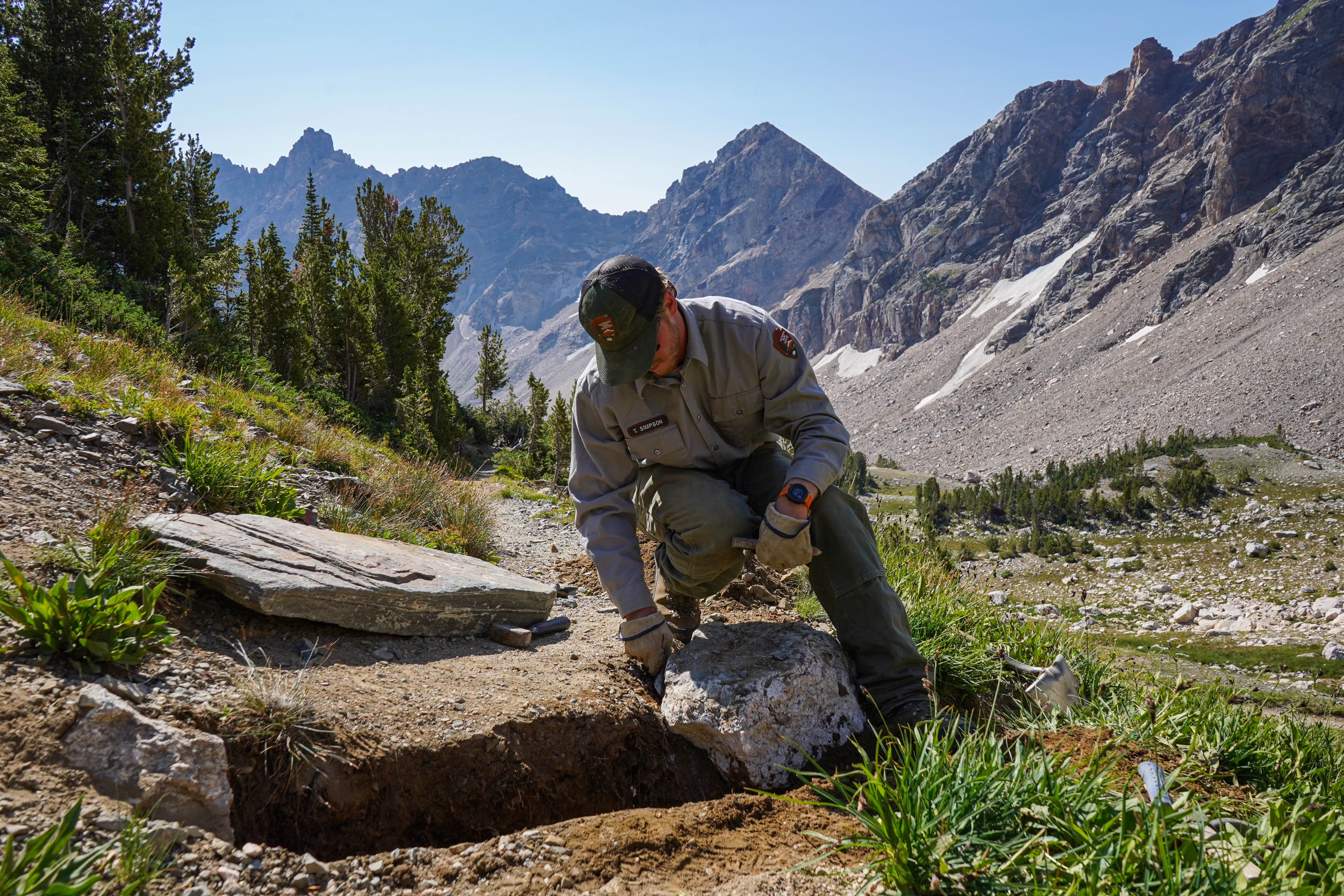 a park employee works on a trail in the mountains