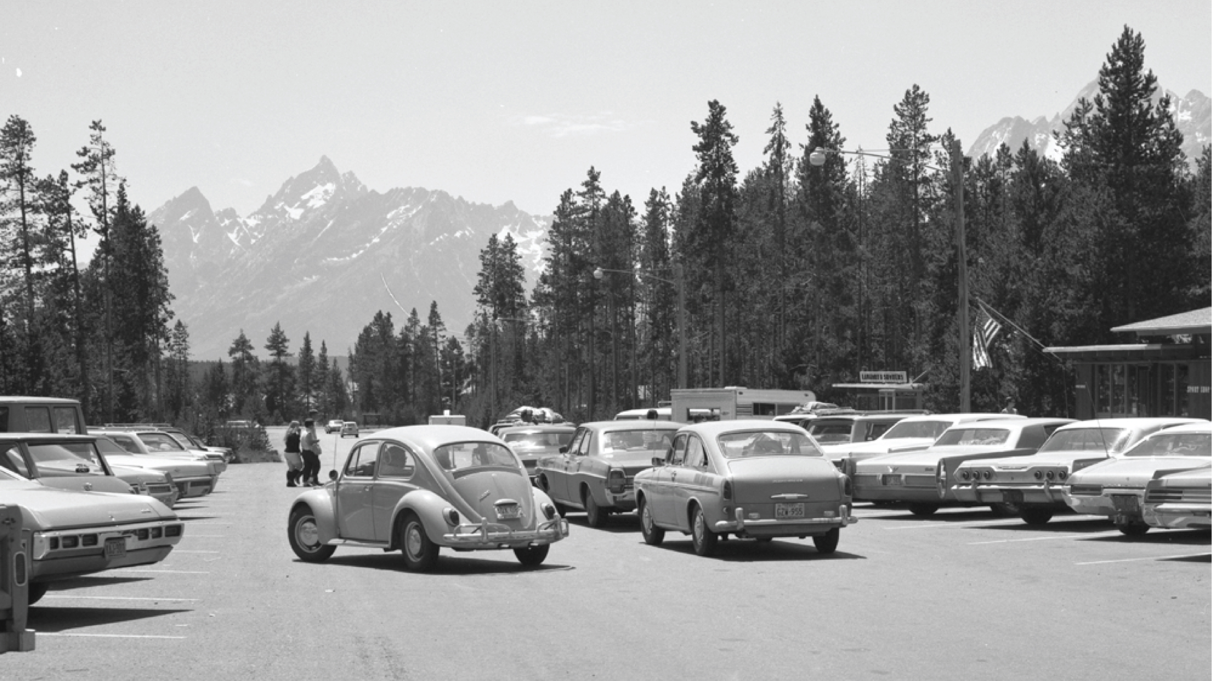 Historic black and white photo of Colter Bay Village parking lot with the Tetons in the distance