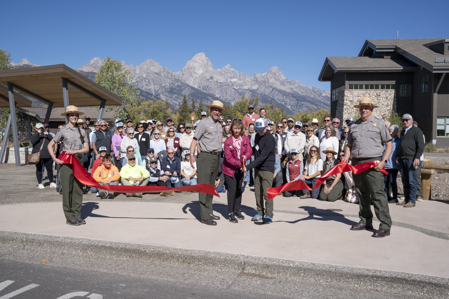 Participants cut a ribbon with spectators and tetons in background