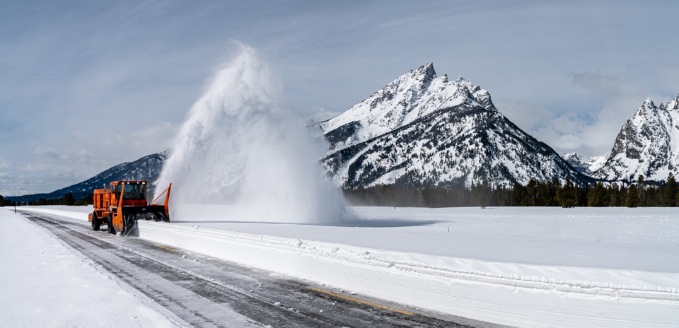 Plows clear snow on the Teton Park Road with the Teton Range in the background and a snow-covered landscape.