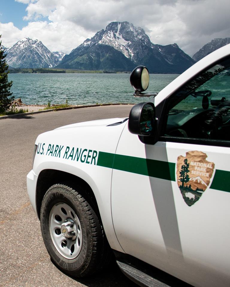 A law enforcement park ranger vehicle parked in front of Jackson Lake with the Teton range in the background