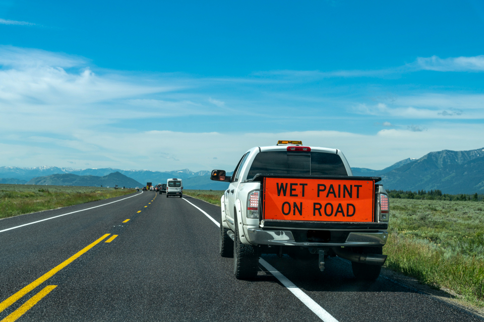 Truck with "Wet paint on road" sign along highway in Grand Teton National Park