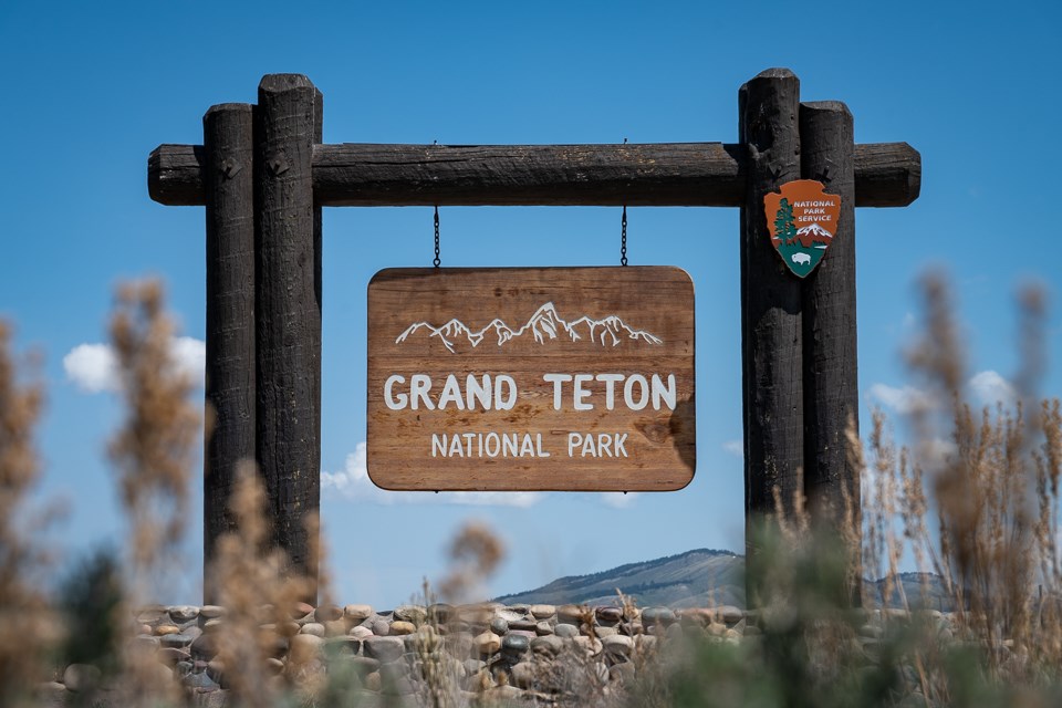 Grand Teton park entrance sign, blue skies, and sage below