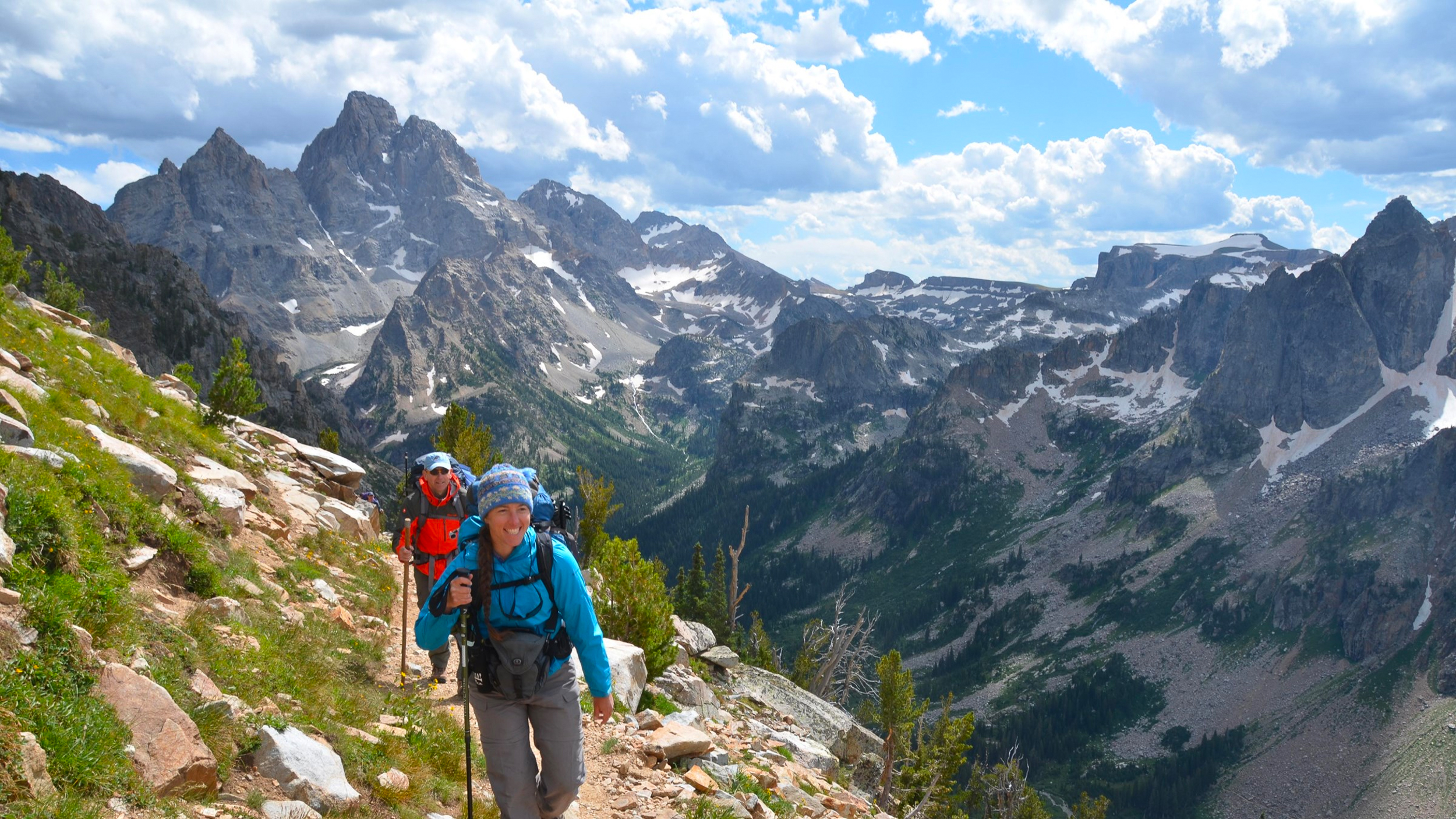 Paintbrush Divide Two hikers walking up a mountain divide with mountains and a canyon behind