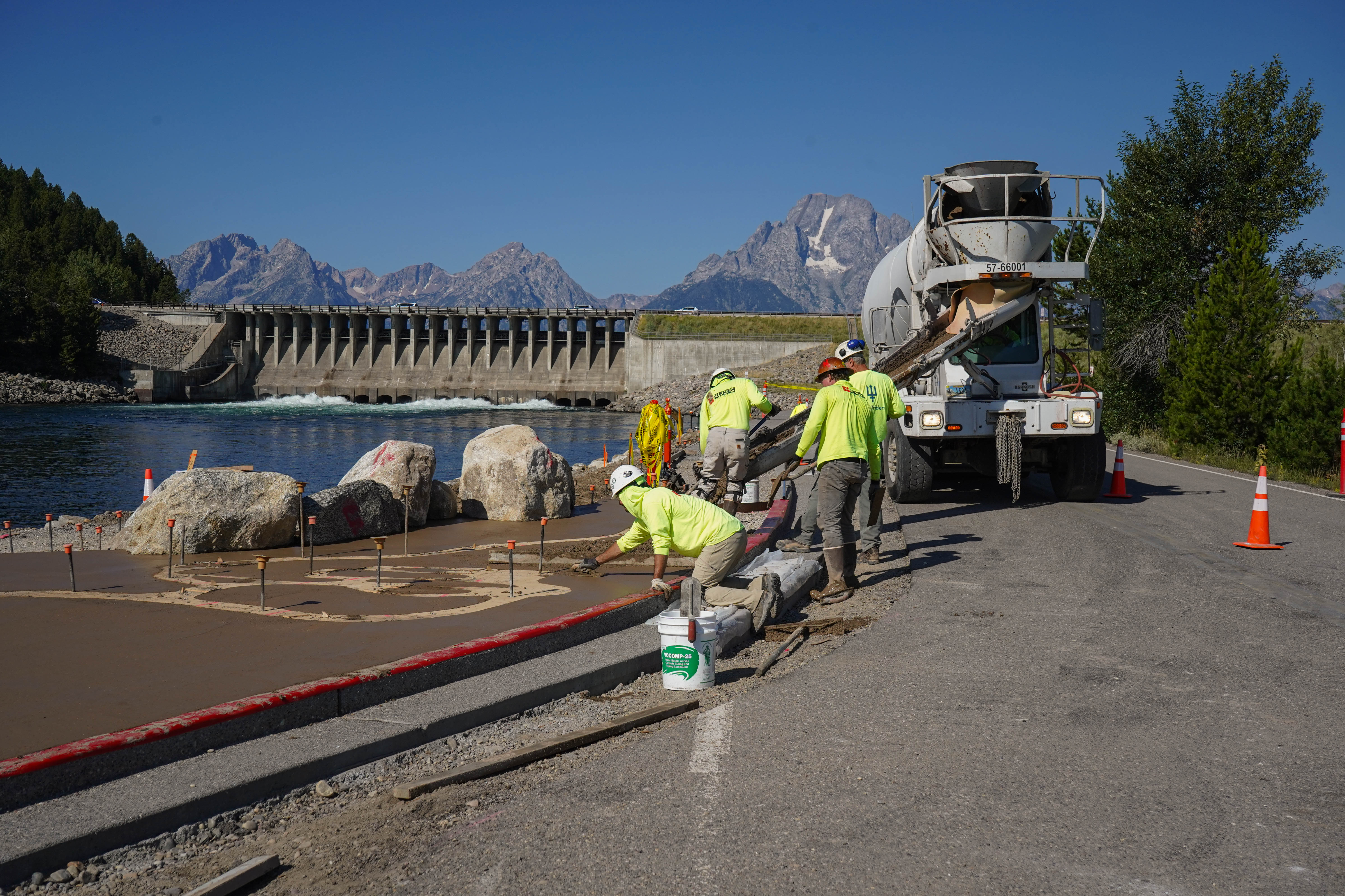 construction workers pour concrete in front of a dam