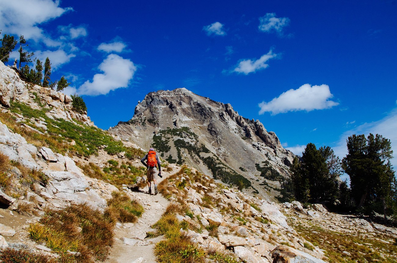 a hiker walks up a trail towards mountains