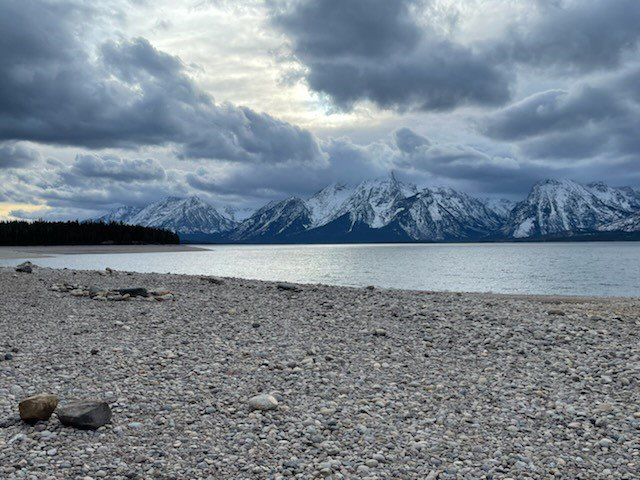 Rocky beach leading up to a lake with the Teton Range in the background.