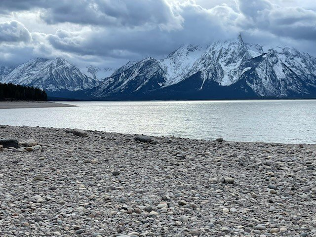 Rocky beach leading up to a lake with the Teton Range in the background.