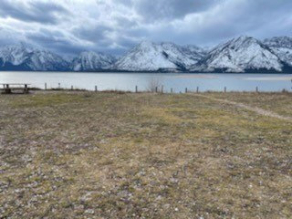 Colter Bay Picnic Level Area 2 A field with a little path off to the right leading up to a body of water with the Teton Range in the background.