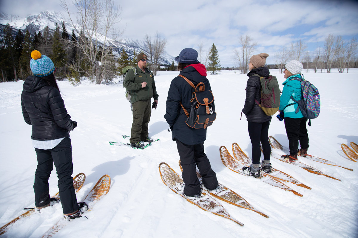 Visitors in snowshoes interacting with a Ranger on snow with mountains behind