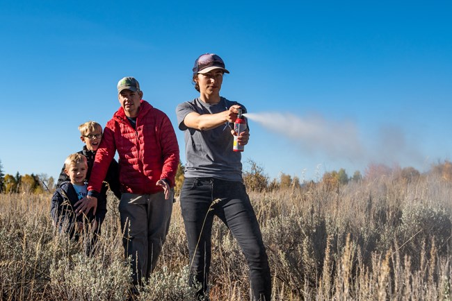 a woman sprays bear spray while a man and two kids stand behind