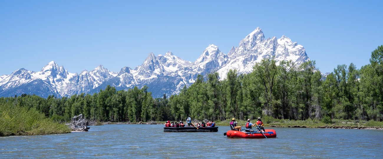 Two rafts float on the Snake River with the Tetons in the background.