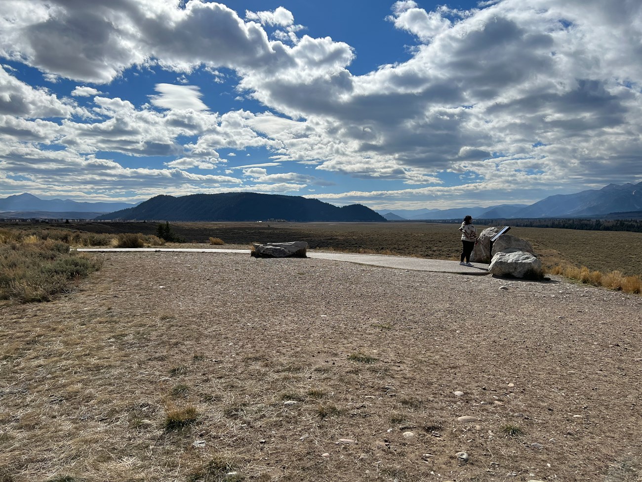 A person standing in front of informational panel with mountain range in background