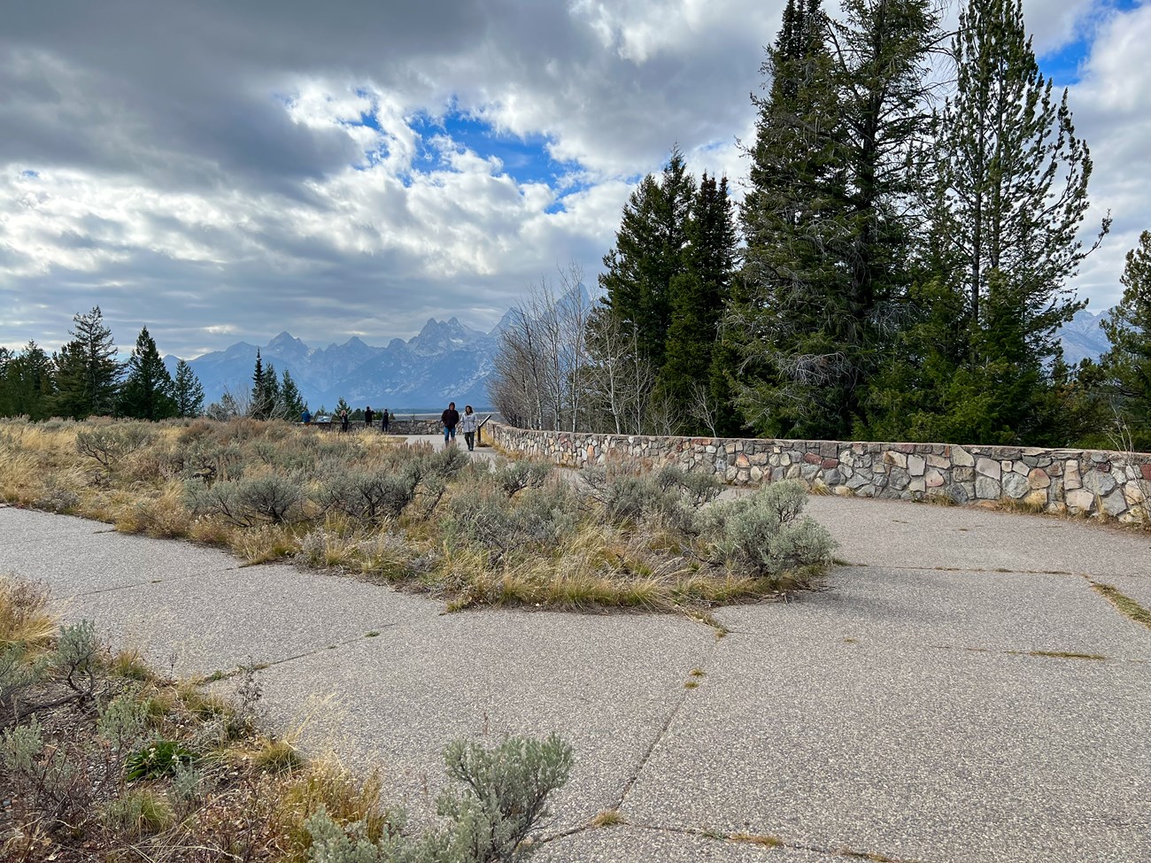 A paved pathway at Snake River Overlook with rock wall and trees in background