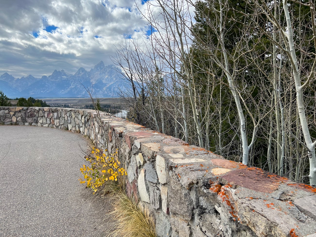Rock wall along paved pathway with Teton range in background