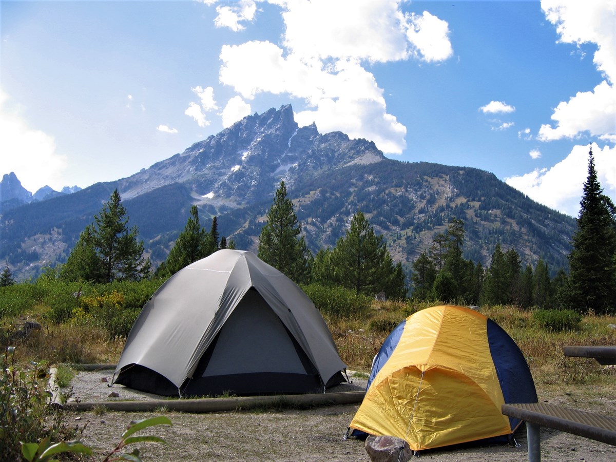 Two tents in a campground in front of a mountain.