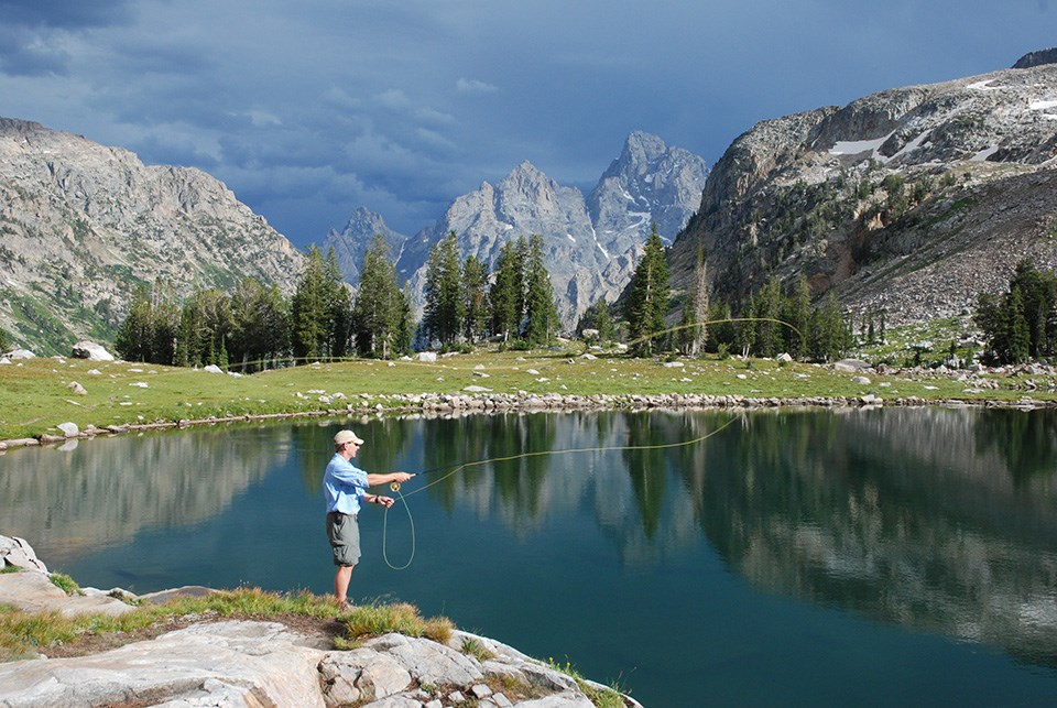 Man fly fishing at Lake Solitude with storm clouds in the distance over the Grand Teton.