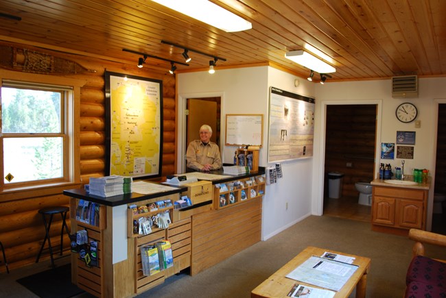 A ranger stands behind a desk in a small building.