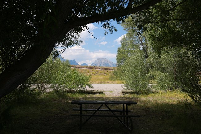A picnic table under trees with mountains in the distance.