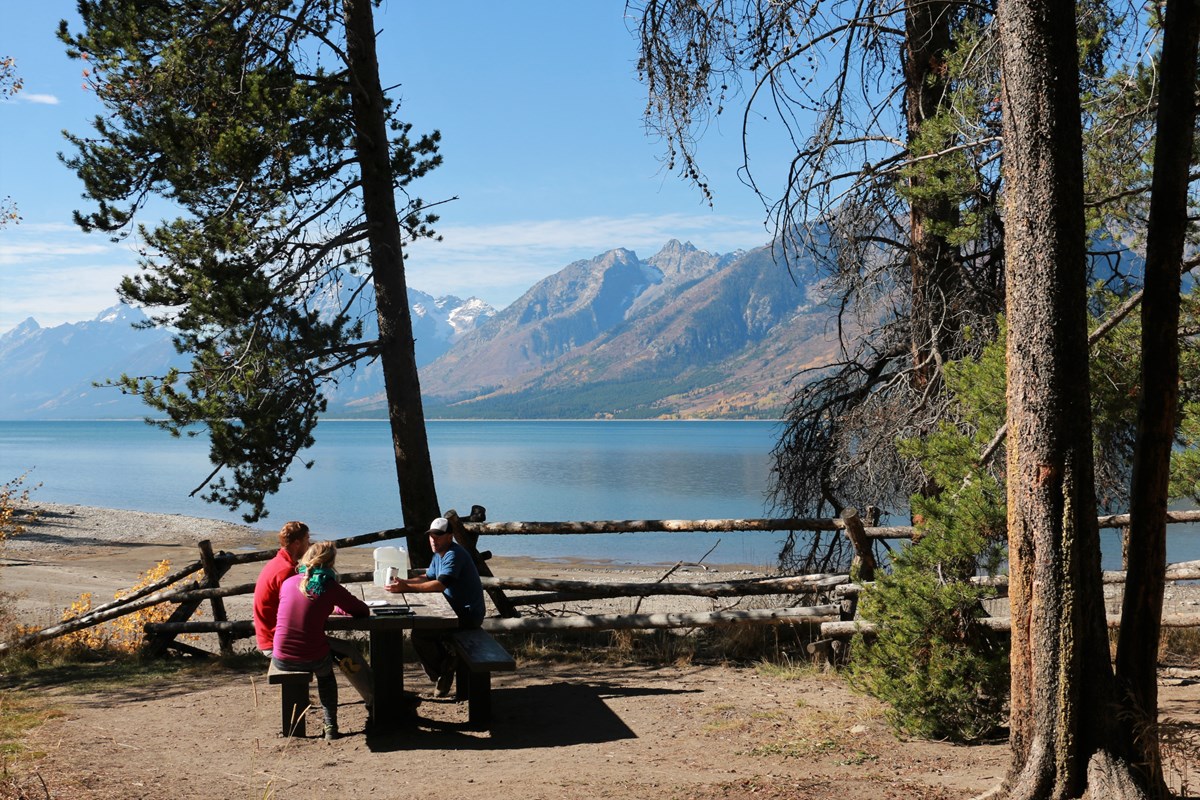 People sit at a picnic table by a lake.