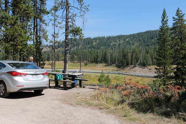 A car parked beside a picnic table under trees.