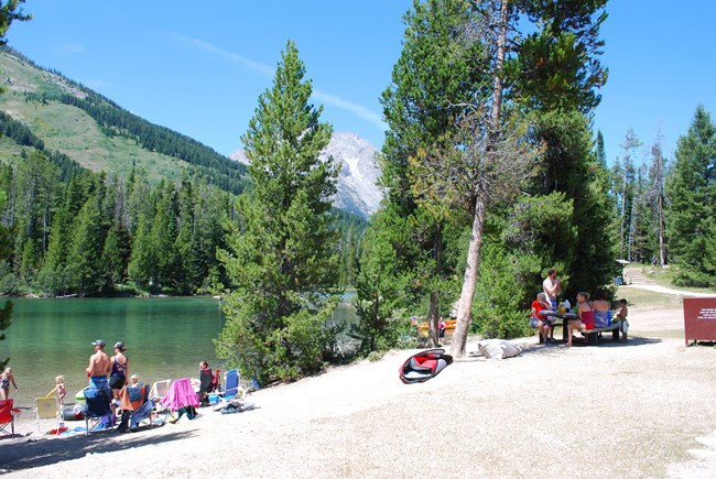Visitors sit at picnic tables by a lake.
