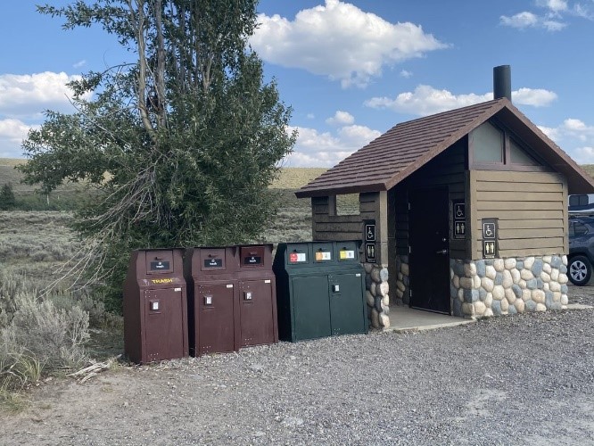 Pit toilet with bearproof trashcans lined to the left of it. 