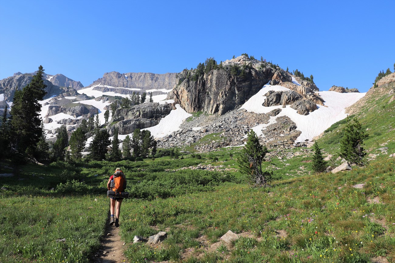 a hiker with a backpack walks along a narrow trail in a mountain canyon