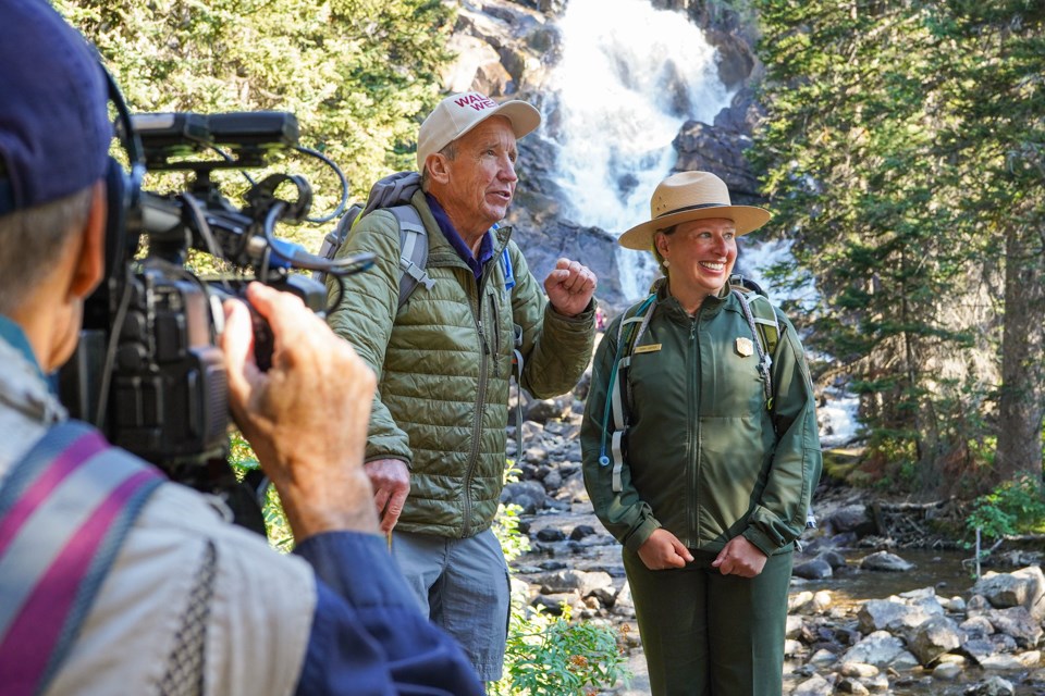 Ranger and television host being filmed by cameraman with waterfall in the background