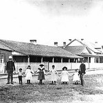 Historic photo of a group in front of wood clap buildings.