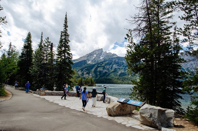 People walk on a paved path by a lake.