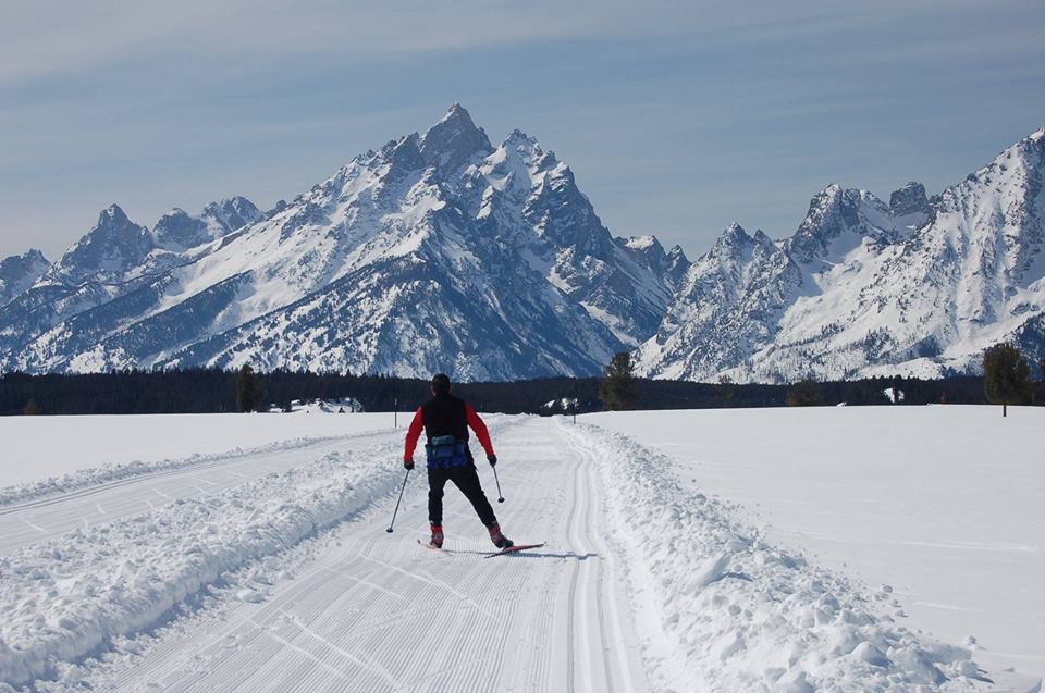 A cross country skier skies down a snow trail towards mountains.